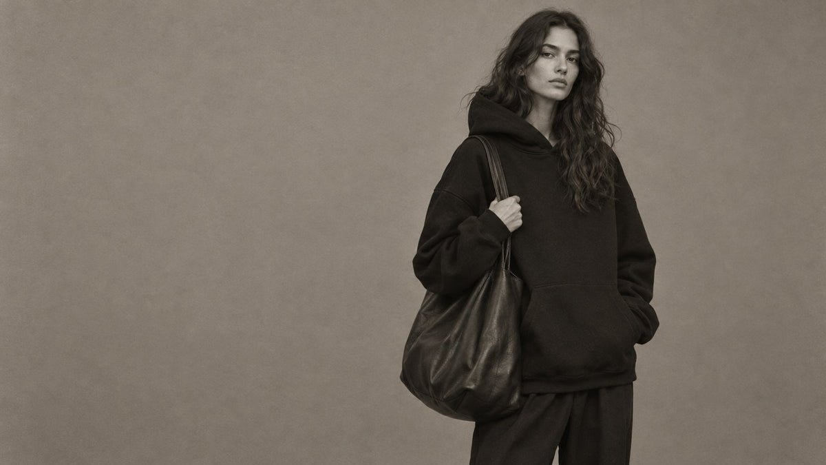 Woman in black hoodie with leather tote against grey backdrop
